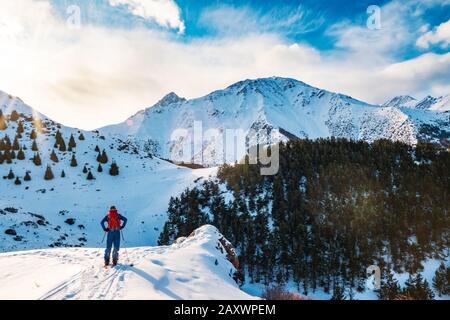 Ski touring on a splitboard. A man stands with his back to the viewer and looks at the mountain landscape. Winter sport. Kyrgyzstan Stock Photo