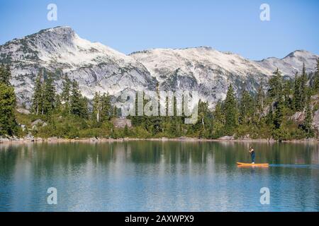 Side view of active woman paddle boarding on mountain lake. Stock Photo