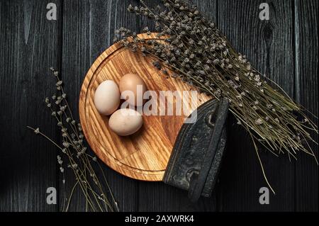 still life of eggs on a black wooden background with dried flowers Stock Photo