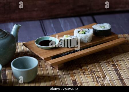 Sushi and soy sauce on wooden stand with chopsticks on bamboo mat. Stock Photo