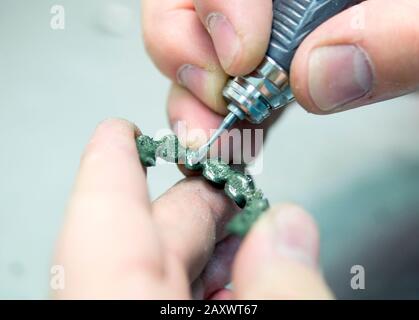 Dentist hand mills tooth crowns created on 3d printer for metal. Dental technician working with ceramic crowns in dental laboratory Stock Photo