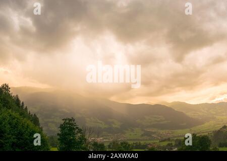 Thunderstorm over a mountain is illuminated from behind by the sun at sunset Stock Photo