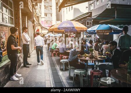 Hong Kong - November, 2019: People sitting in crowded street food restaurant eating lunch  in Soho, Hong Kong Stock Photo