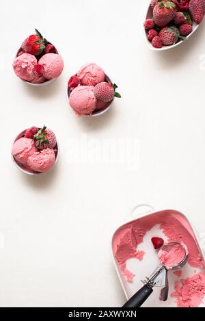 Scoops of raspberry ice cream in white bowls with frozen raspberry and strawberries on a white table. Above view of homemade berries ice cream. Stock Photo