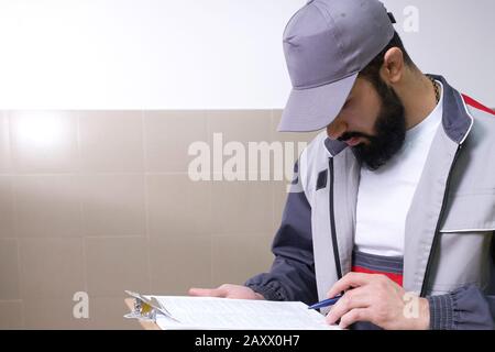Concentrated young technician wearing overall standing and taking some notes Stock Photo