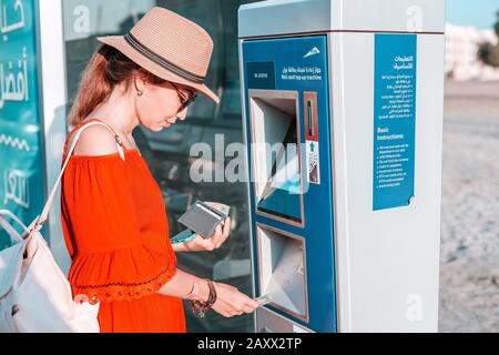 28 November 2019, UAE, Dubai: Tourist girl top up her Nol transport card in Atm terminal near bus stop Stock Photo