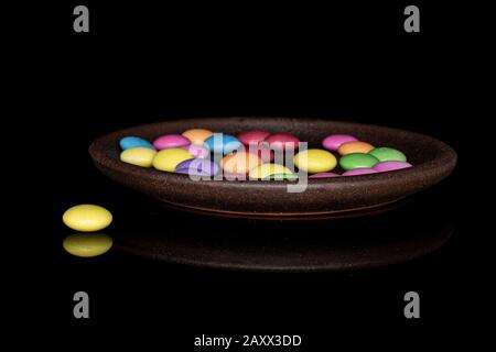 Lot of whole sweet colourful candy with brown ceramic coaster isolated on black glass Stock Photo