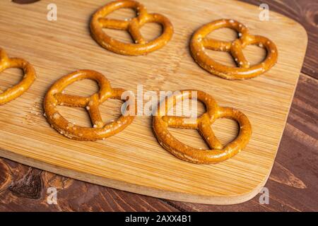 Group of four whole salty brown pretzel on bamboo cutting board on brown wood Stock Photo