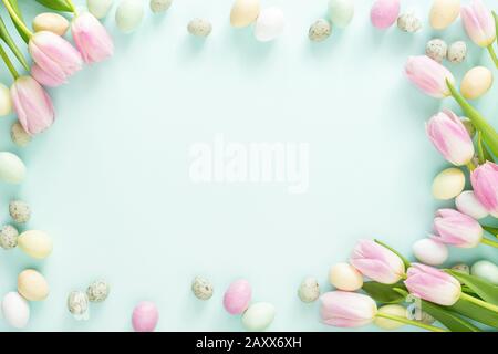 Colored Easter candy eggs and pink tulips on turquoise background. Easter frame. Stock Photo