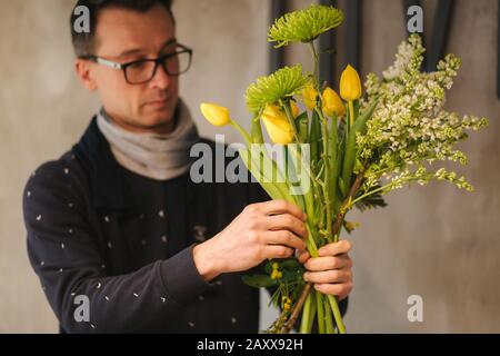 Flowers delivery shop. Florist creating order, making spring bouquet. Male make bouquet using yellow tulips Stock Photo