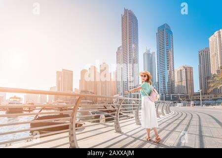 Cheerful asian traveler girl walking on a promenade in Dubai Marina district. Travel destinations and tourist lifestyle in UAE Stock Photo