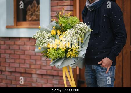 Stylish man in glasses hold bouquet of flower outside. Background of brick wall Stock Photo