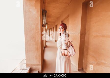 Follow happy woman traveler wearing dress and turban walking through the streets of an old Arab town or village in the middle of the desert. Concept o Stock Photo