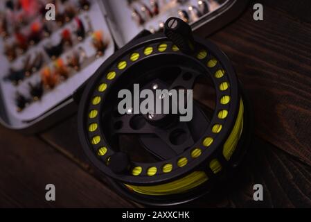 Fly Fishing reel and box of flies on wooden surface Stock Photo