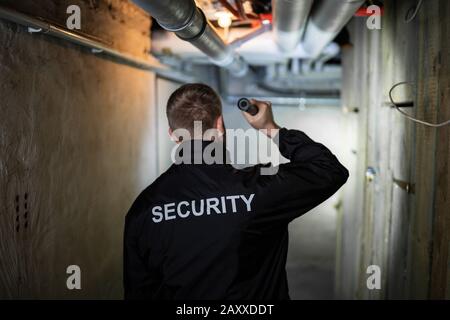 Rear View Of A Security Guard Standing In The Basement Holding Flashlight Stock Photo