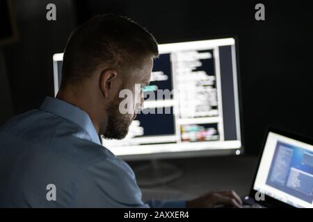 Programmer Working Late At Night On Multiple Computer Screens Stock Photo