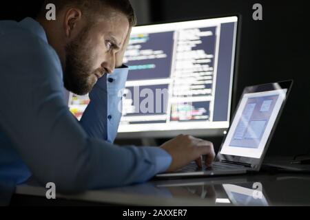 Worried Programmer Working Late At Night On Multiple Computer Screens Stock Photo