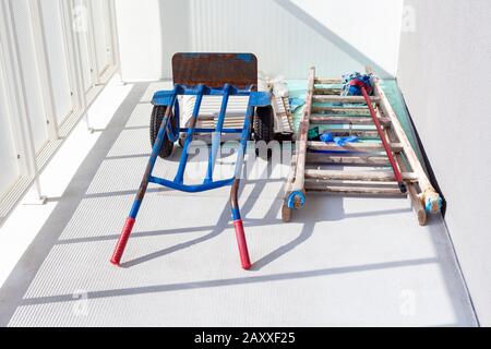 Handtruck and a wooden painter ladder and a mop laying on the white balcony. House or flat under construction abstract concept. Construction job Stock Photo