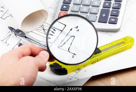 Scientist, architect or electrician holding a magnifying glass and inspecting analyzing data on a graph, chart. Engineering abstract concept, notes Stock Photo