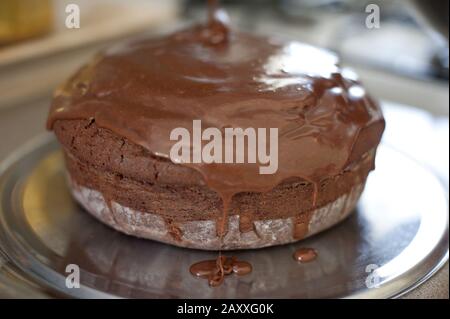 Freshly poured chocolate icing dripping off a home baked cake on a metal tray in a close up view Stock Photo