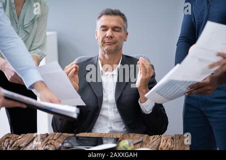 Mature Businessman Meditating While Surrounded By His Executives Stock Photo