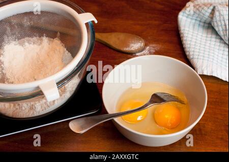 https://l450v.alamy.com/450v/2axxgtc/fresh-baking-ingredients-with-two-eggs-in-a-mixing-bowl-and-sifted-white-cake-flour-in-a-sieve-on-a-wooden-kitchen-counter-2axxgtc.jpg