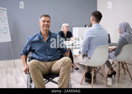 Mature Disabled Businessman Sitting On Wheelchair Working In Office Stock Photo