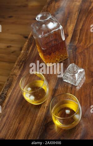 Two glasses of Scotch on the rocks served with ice and an open cut glass decanter alongside, view from above on a wooden bar counter Stock Photo