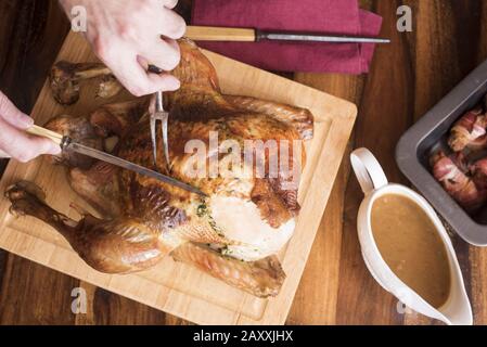 Person carving roasted thanksgiving turkey on wooden board Stock Photo