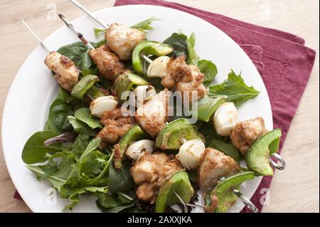 Three Chicken and bell pepper shish kebabs on a bed of lettuce leaves placed in a round white plate Stock Photo
