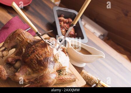 Delicious roast Christmas dinner meat with a partially carved turkey and pan with bacon rolls alongside gravy in a sauce boat Stock Photo
