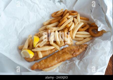Overhead view of fried fish fillets in batter, calamari rings and potato chips on crumpled paper Stock Photo