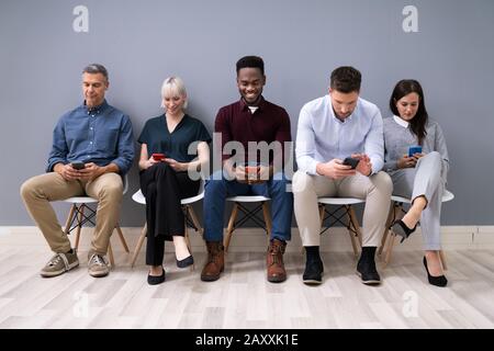 Business People Sitting On Chairs Using Smartphones In Office Stock Photo