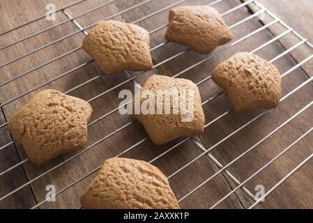 Batch of fresh baked star shaped gingerbread Christmas cookies cooling on a wire rack on a wooden kitchen table viewed high angle Stock Photo