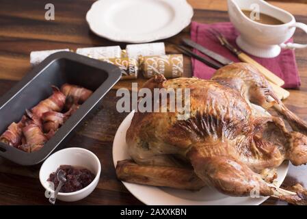 Crispy brown roast turkey for Christmas dinner with bacon rolls and cranberry sauce ready for carving on a table Stock Photo