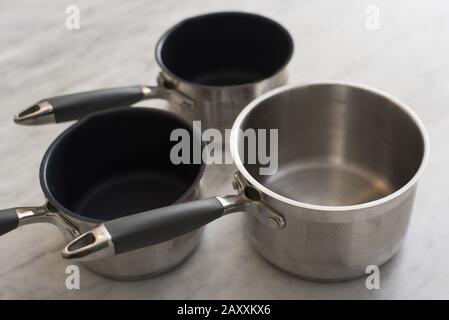 Three empty clean metal saucepans on a kitchen counter, two of which are non-stick and one stainless steel Stock Photo