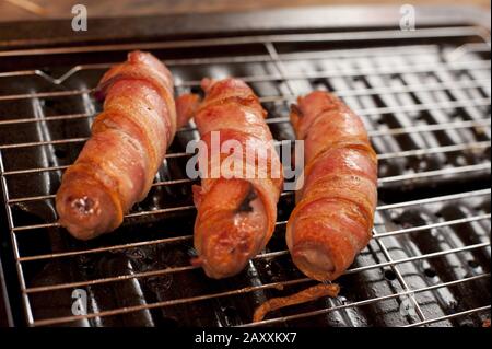 Pork sausage and bacon rolls, or traditional pigs in blankets, on a grill in close up
