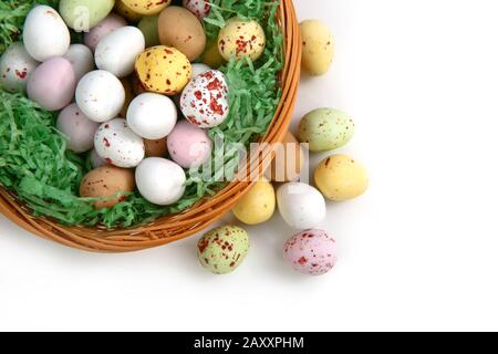 Chocolate mini Easter eggs in straw or whicker basket against a white background Stock Photo