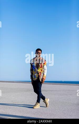 Front view of a young black man wearing eyeglasses standing against blue sky while looking camera Stock Photo