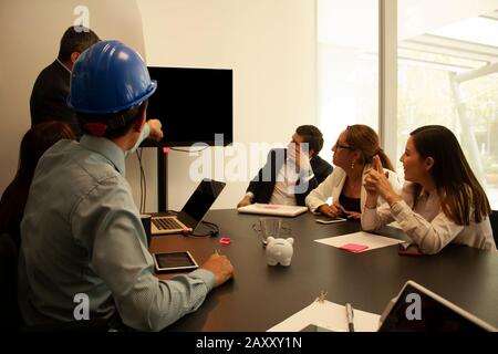 Architect asking the boss about the presentation he exposes while the rest of his co-workers are in the office paying attention to the boss in offices Stock Photo