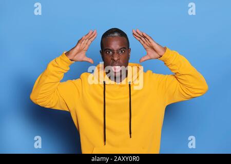 Portrait of black male standing against blue background with hand next to the heat in pain an stress Stock Photo