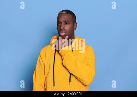 Portrait of serious thoughtful male wears casual clothes, has pensive expression, isolated over blue background. African American plump man thinks abo Stock Photo