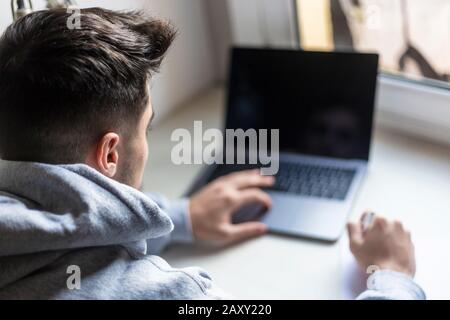 Rear view of a young man working with laptop on desktop Stock Photo