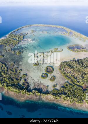 A remote tropical island in the Molucca Sea is fringed by a ring of mangrove forest that surrounds a shallow lagoon. Stock Photo