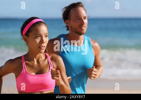 Couple runners running on beach. Interracial young adults asian woman, caucasian man, training cardio together doing outdoor workout jogging. Stock Photo