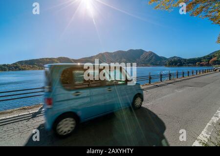 Eco car driving on road with lake and mountain landscape scenery. Motion blur showing car movement. Concept of road trip travel, rental cars, green en Stock Photo