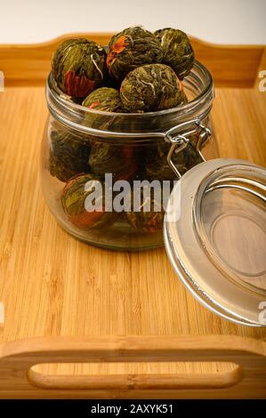 A ball of flower tea in a glass jar on a wooden tray on a white background. Close up Stock Photo
