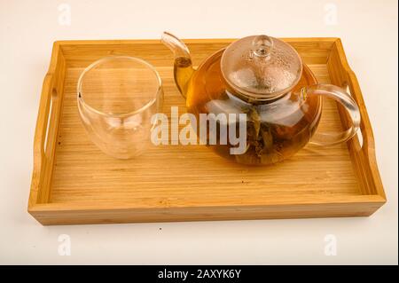 Flower tea brewed in a glass teapot and a glass on a wooden tray on a white background. Close up Stock Photo