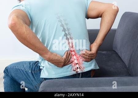 Mature Man Sitting On Sofa Suffering From Back Pain Stock Photo
