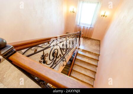 wrought iron staircase in the cottage. Marble steps, black wrought iron stairs with floral ornaments. Mahogany wooden railing. The staircase between f Stock Photo
